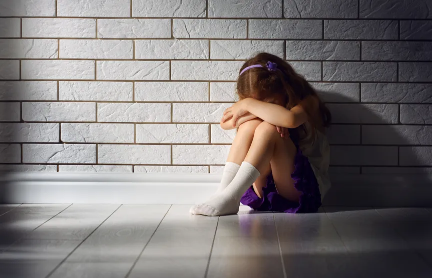 Mädchen sitzt mit angezogenen Knien allein an einer Wand